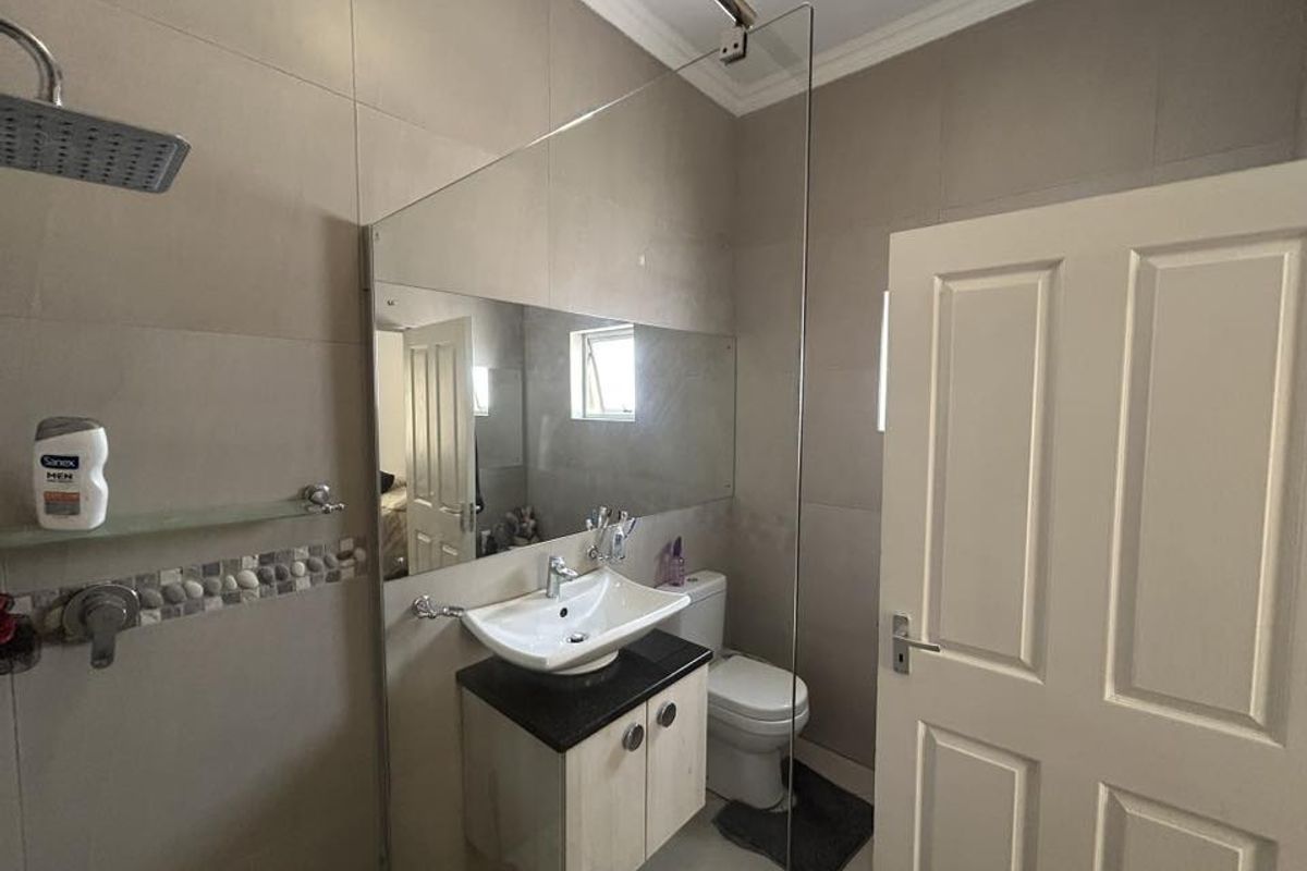 A functional bathroom featuring a glass-enclosed shower, a modern vanity with a basin, and a toilet, finished with neutral wall tiles.