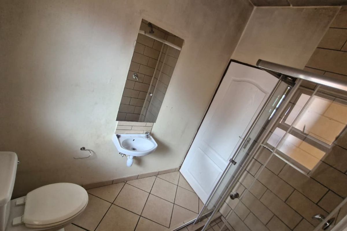 A functional bathroom featuring a shower enclosure, wall-mounted basin with mirror, and toilet, finished with tiled flooring and partial wall tiling.