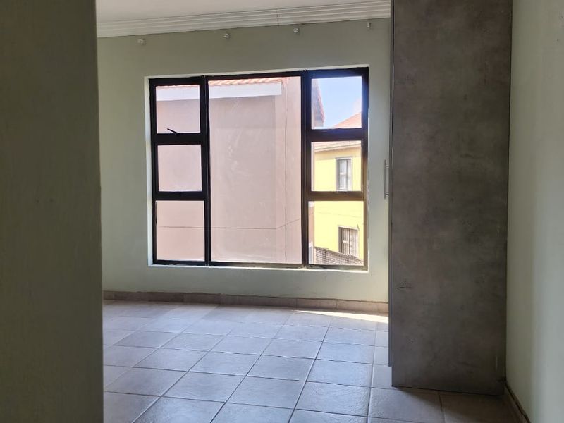 An empty bedroom featuring tiled flooring, a built-in cupboard, and large aluminium-framed windows providing natural light.
