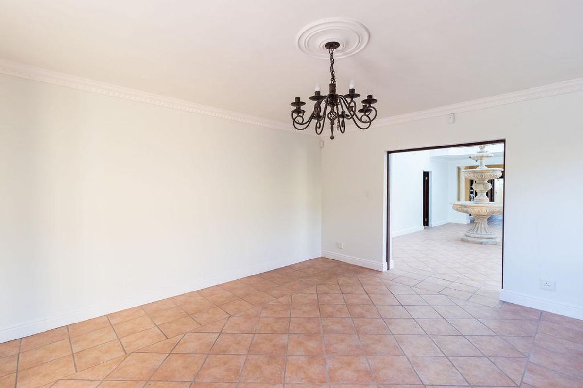 A spacious, empty living area featuring terracotta floor tiles, crown molding, and a decorative wrought iron chandelier, leading into an adjacent foyer.