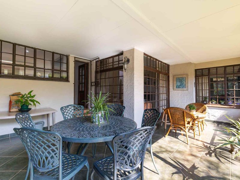 A covered outdoor patio area featuring tiled flooring and large metal-framed windows, providing a functional space for outdoor dining and relaxation.