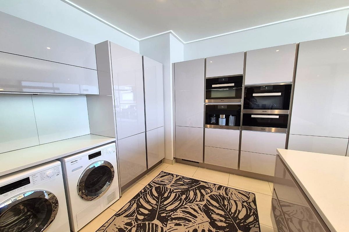 Modern kitchen featuring high-gloss cabinetry, integrated Miele appliances, built-in oven and microwave, and sleek stone countertops in a clean, contemporary layout.