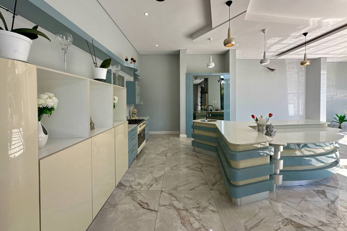 Modern kitchen featuring a large curved island with stone countertops, integrated cabinetry, and marble-style floor tiling in an open-plan layout.