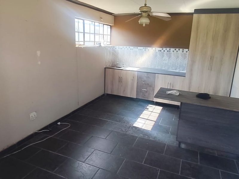 A functional kitchen area featuring built-in cabinetry, a tiled backsplash, and dark floor tiles, offering a blank canvas for potential updates.