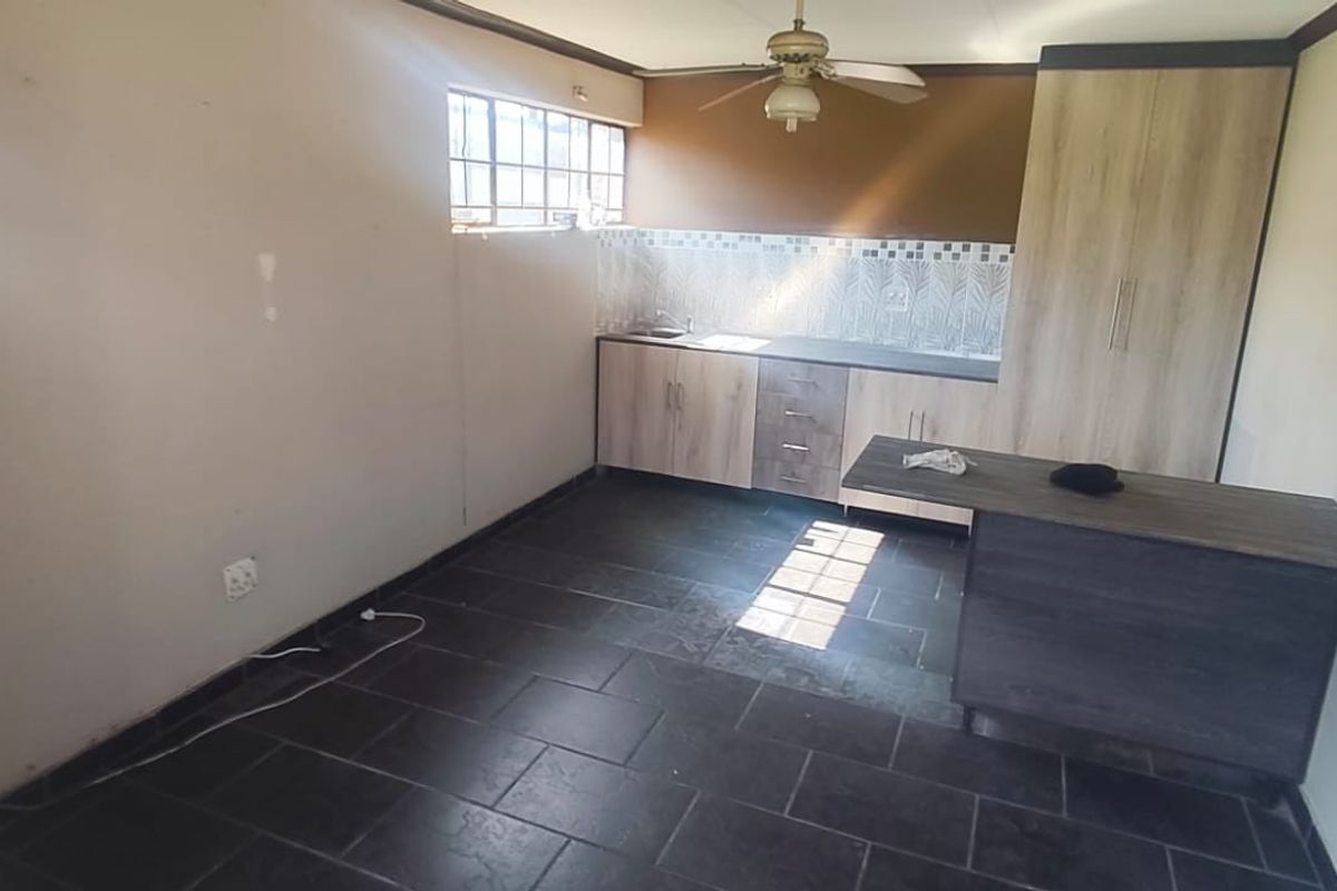 A functional kitchen area featuring built-in cabinetry, a tiled backsplash, and dark floor tiles, offering a blank canvas for potential updates.