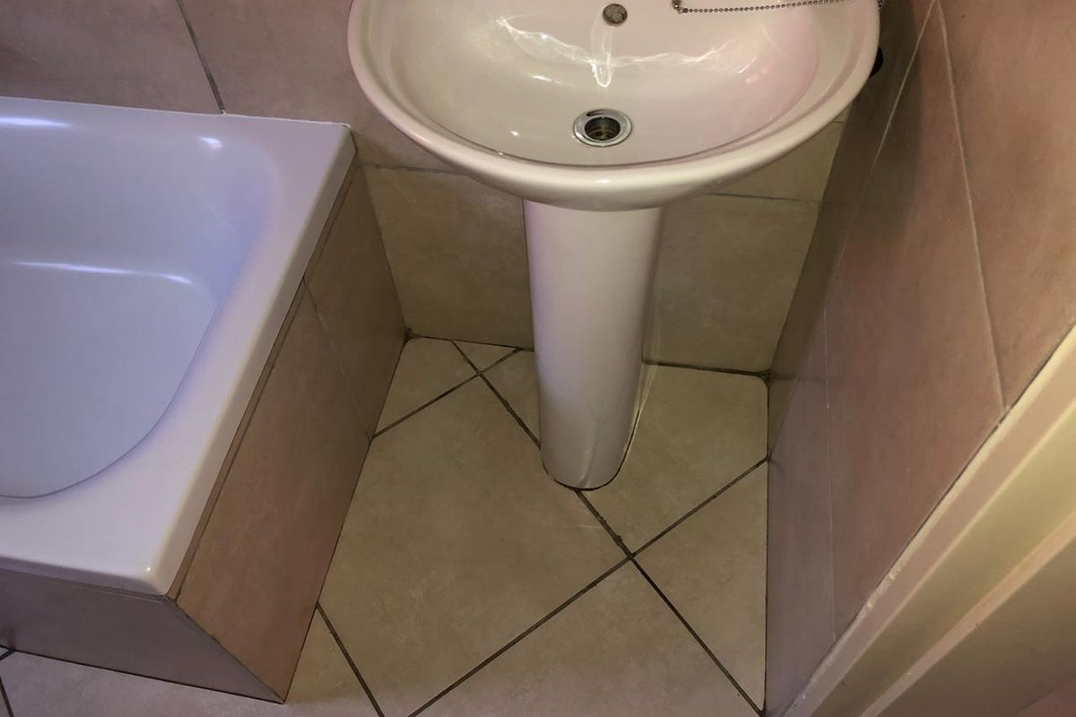 A compact bathroom featuring a white pedestal basin and a built-in bathtub with tiled surrounds and flooring.