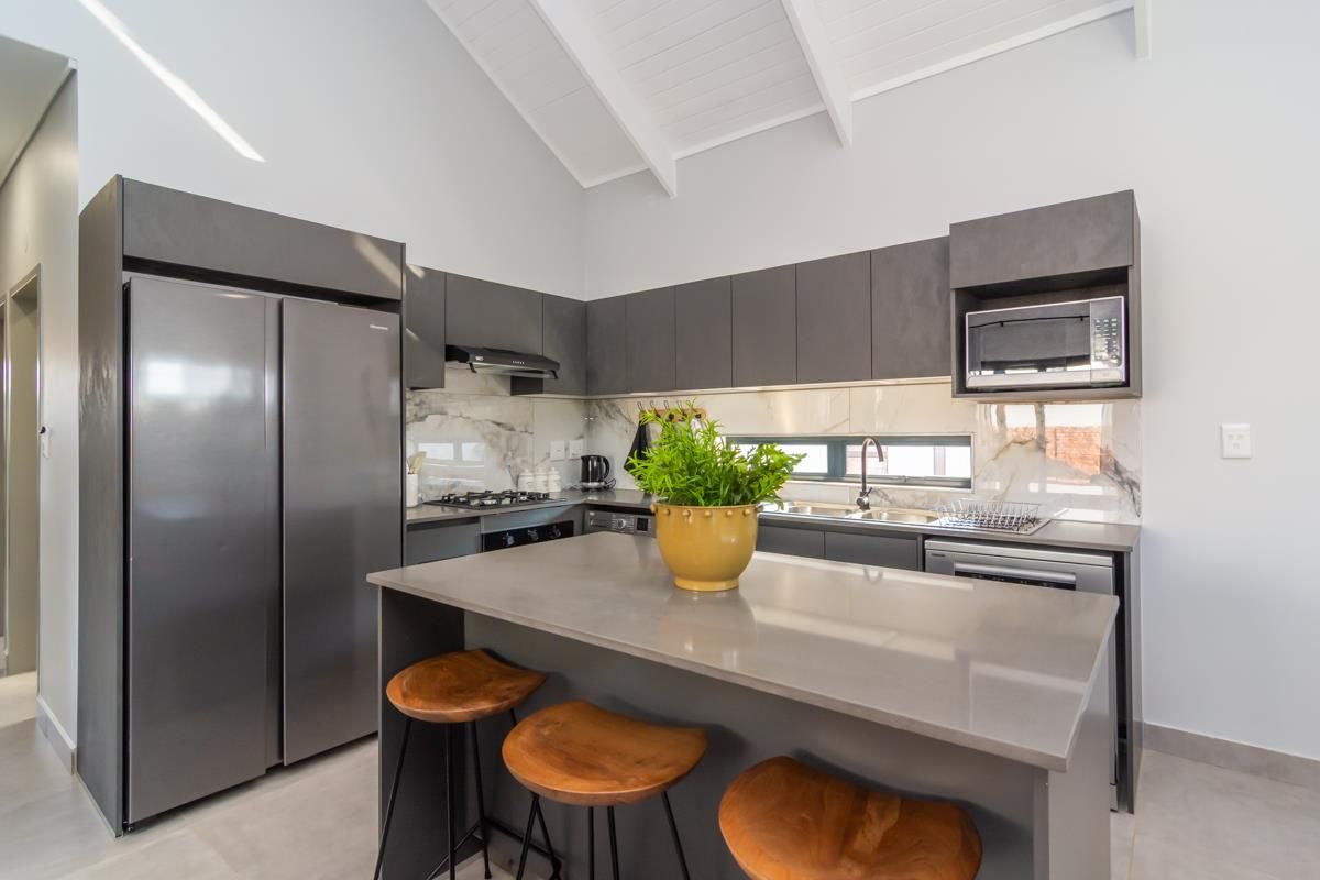 Modern kitchen featuring dark grey cabinetry, stone countertops, a central island, and a vaulted ceiling with high-end finishes and integrated appliances.
