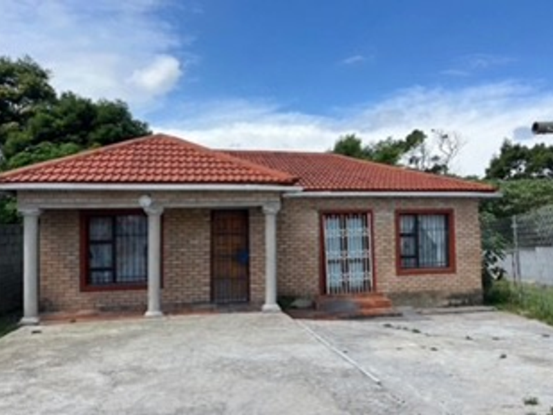 Front elevation of a single-story brick house featuring a tiled roof, covered porch with columns, and a concrete driveway with security features.