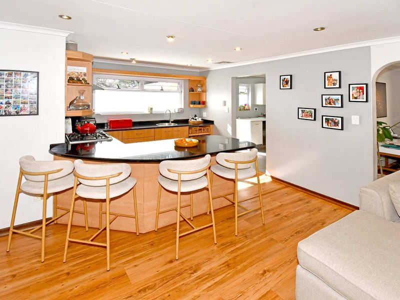Open-plan kitchen and living area featuring a central island with granite countertops, recessed lighting, and warm-toned laminate flooring.