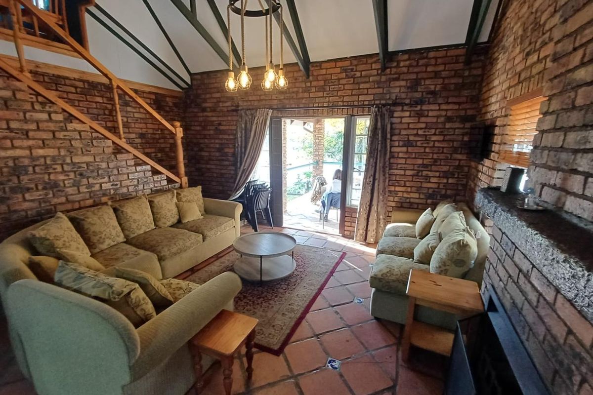 Spacious living room featuring exposed brick walls, vaulted ceilings with exposed beams, terracotta floor tiles, and a built-in fireplace with direct patio access.