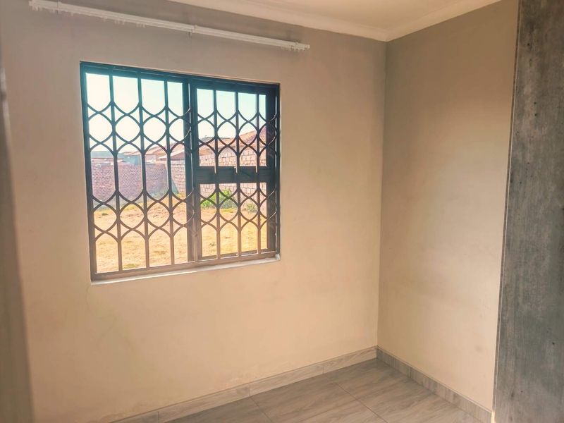 A clean, empty bedroom featuring tiled flooring and a window fitted with a security gate.