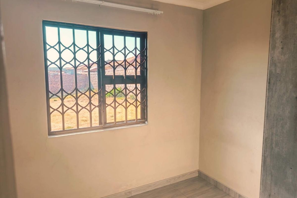 A clean, empty bedroom featuring tiled flooring and a window fitted with a security gate.