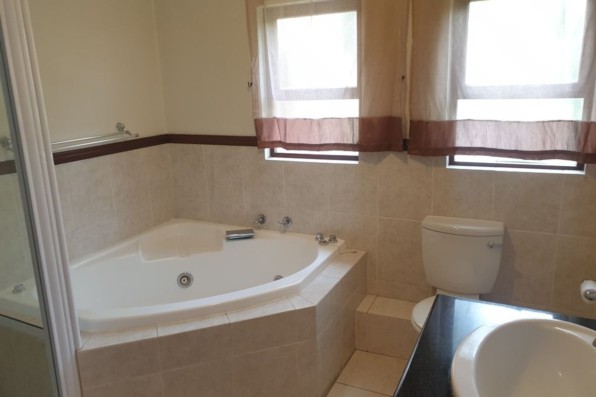 A functional bathroom featuring a corner bathtub, toilet, and vanity basin with tiled finishes throughout.