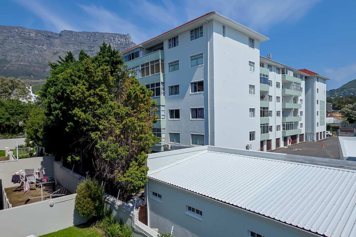 Exterior view of a multi-story apartment building featuring balconies, a metal roof, and a paved driveway area with mountain views.