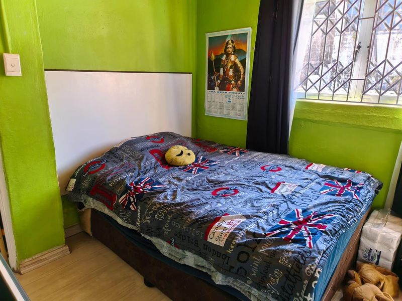 A bedroom featuring laminate flooring, a built-in headboard, and a security gate on the window. The room requires cosmetic updates to the wall finishes.