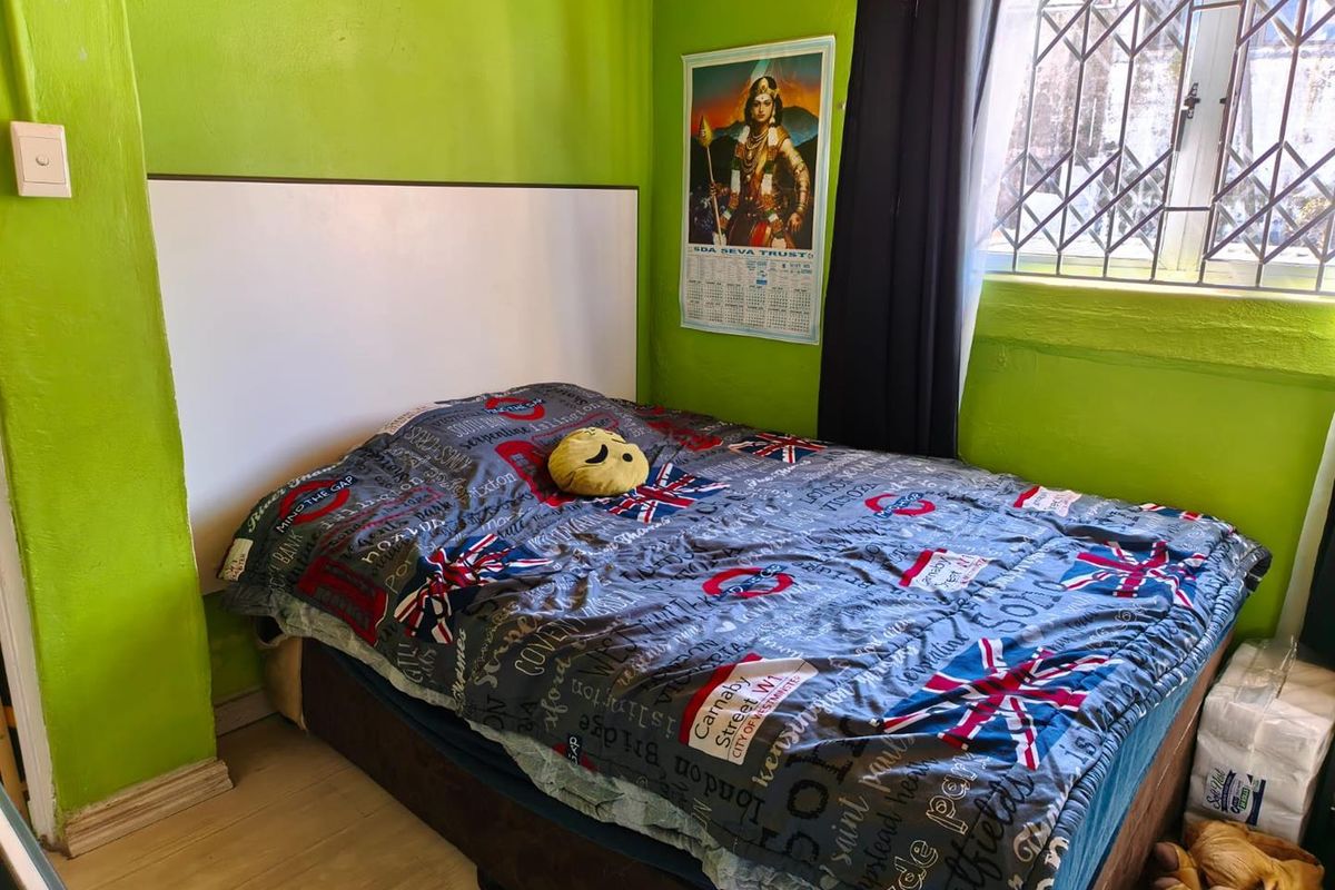 A bedroom featuring laminate flooring, a built-in headboard, and a security gate on the window. The room requires cosmetic updates to the wall finishes.