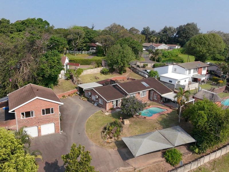 Aerial view of a residential property featuring a main house, detached double garage, swimming pool, and paved driveway set within a landscaped garden.