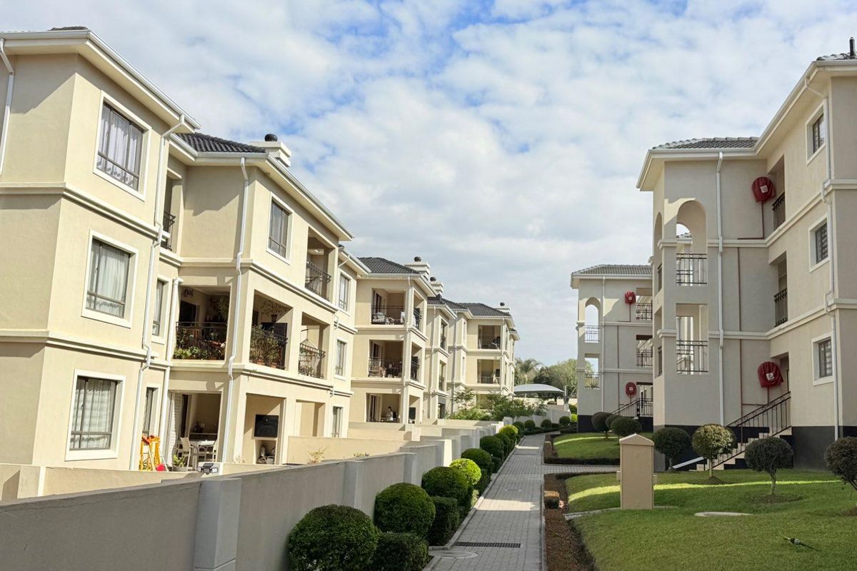 Exterior view of a modern apartment complex featuring multi-story buildings, paved walkways, and well-maintained landscaped garden areas.