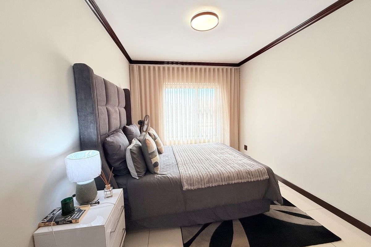A well-maintained bedroom featuring tiled flooring, crown molding, and large window with integrated curtain tracks.