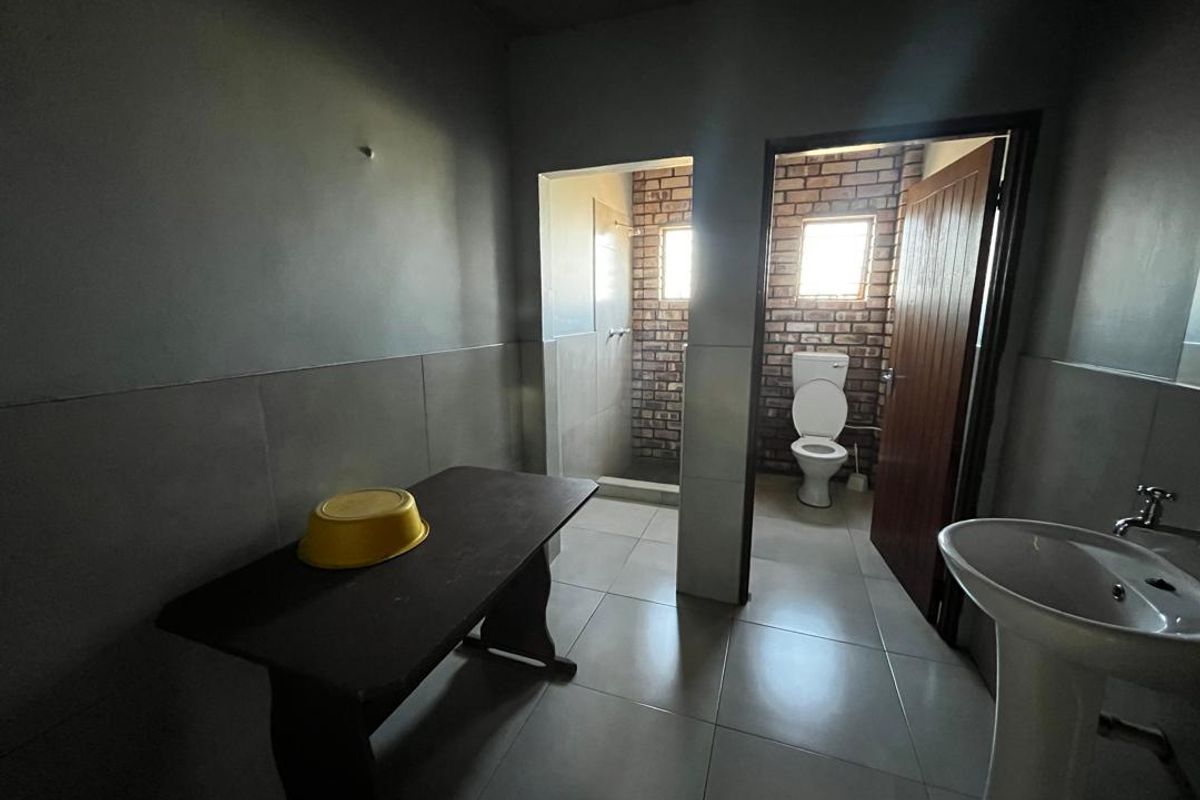 A functional bathroom featuring a pedestal basin, separate toilet area with exposed brickwork, and a shower cubicle with tiled flooring.