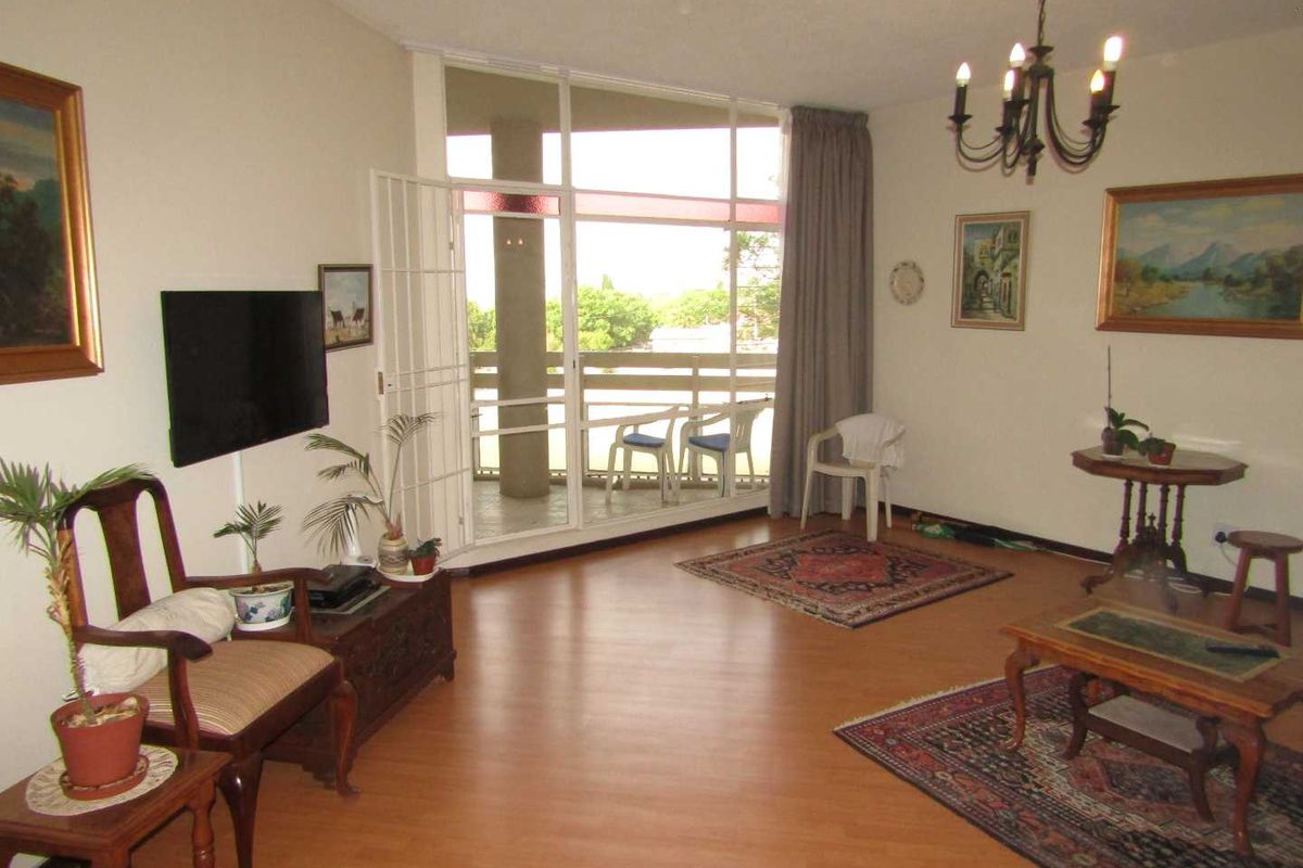 Spacious living room featuring laminate flooring, a classic chandelier, and large glass sliding doors leading to a private balcony.