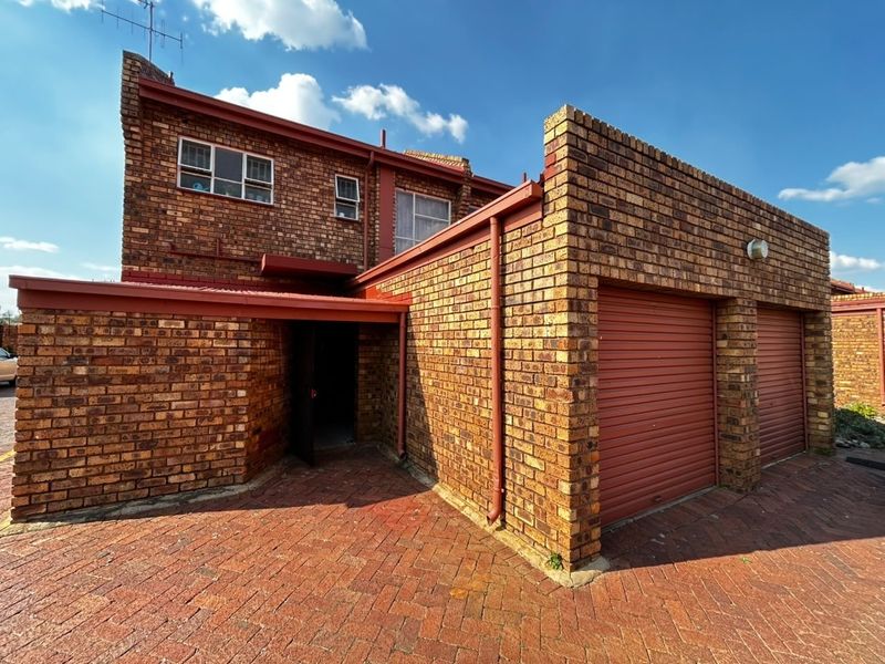Front exterior view of a face brick townhouse featuring a double garage with roller shutter doors and a paved driveway entrance.