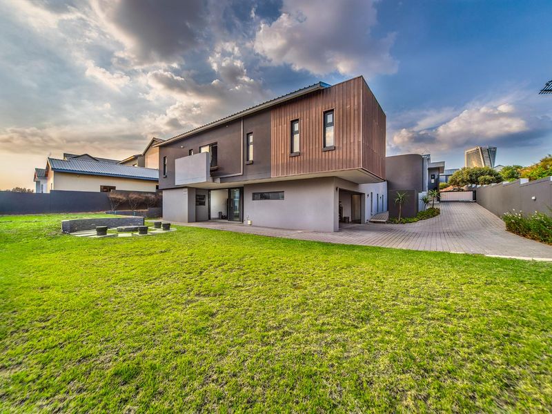 A modern two-story residential property featuring timber cladding, a spacious rear lawn, and a paved driveway leading to a covered parking area.