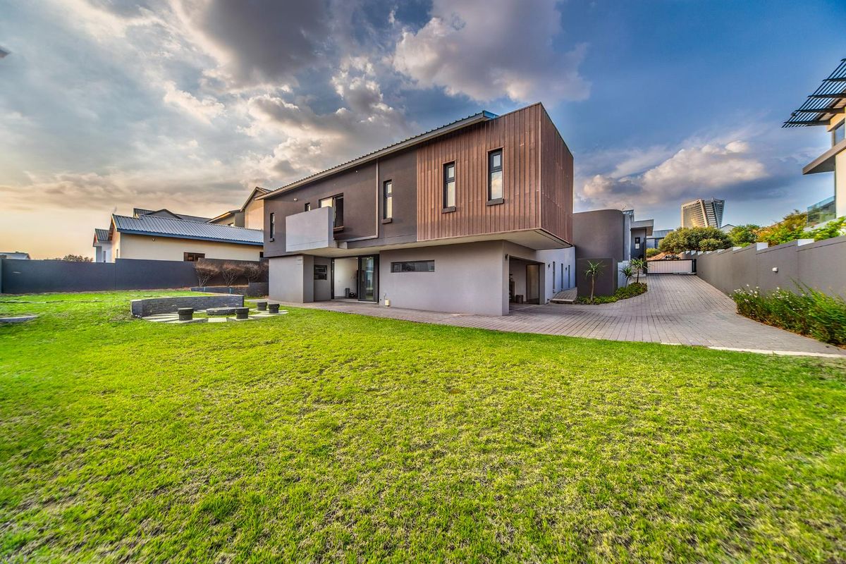 A modern two-story residential property featuring timber cladding, a spacious rear lawn, and a paved driveway leading to a covered parking area.
