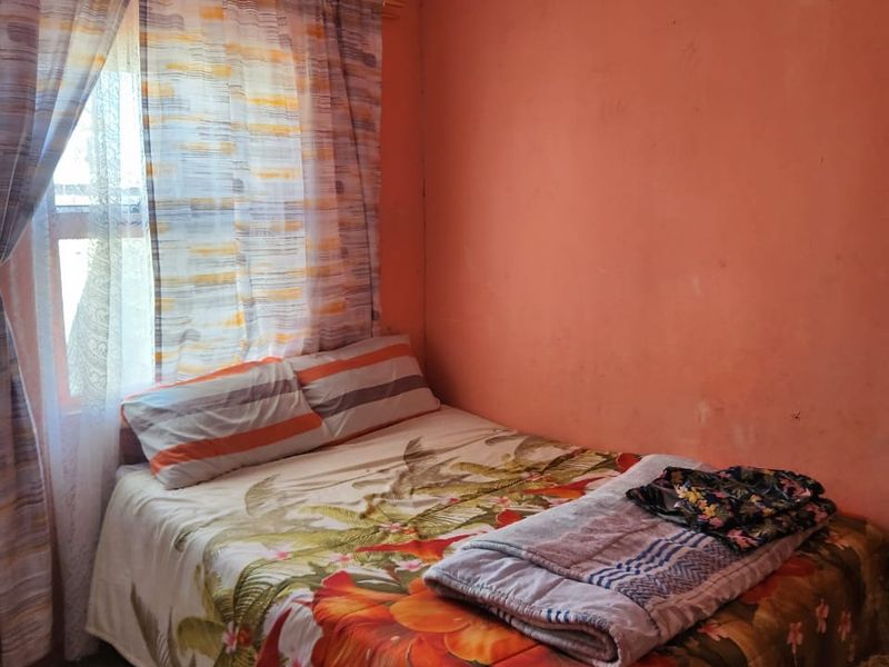 A compact bedroom featuring tiled flooring and a window, currently requiring cosmetic updates to the wall finishes to improve the overall aesthetic.