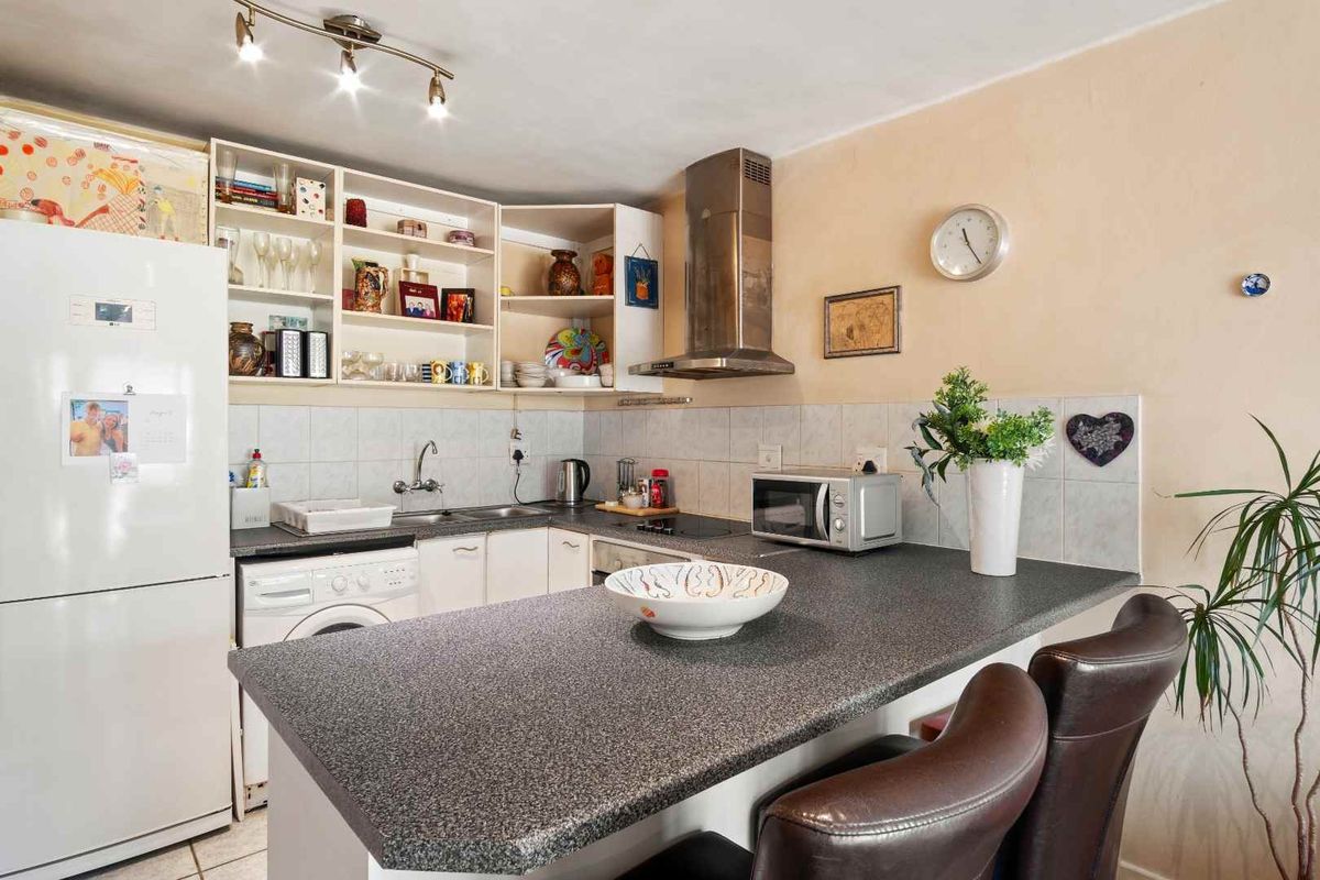 Compact kitchen featuring built-in cabinetry, a stainless steel extractor fan, tiled backsplash, and a breakfast bar with laminate countertop.