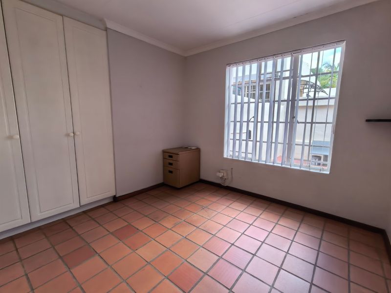 A bright, empty bedroom featuring built-in cupboards, tiled flooring, and security bars on the window.