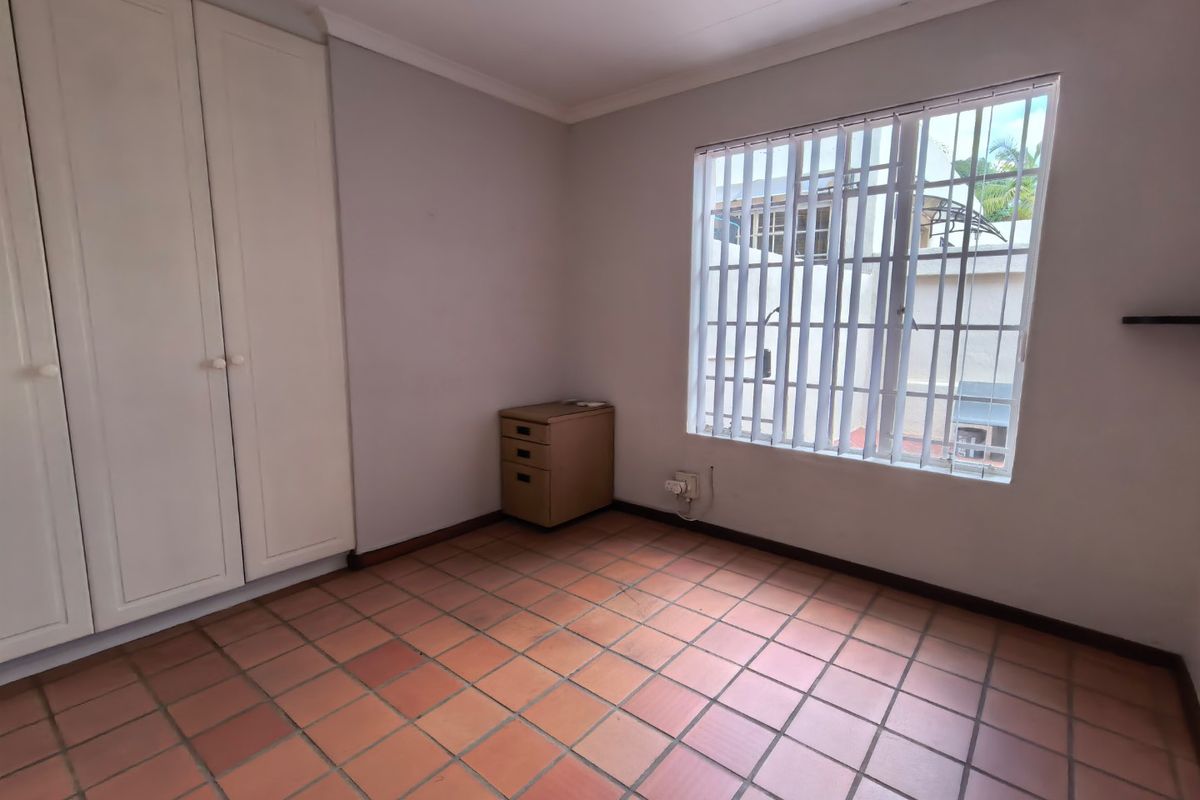 A bright, empty bedroom featuring built-in cupboards, tiled flooring, and security bars on the window.