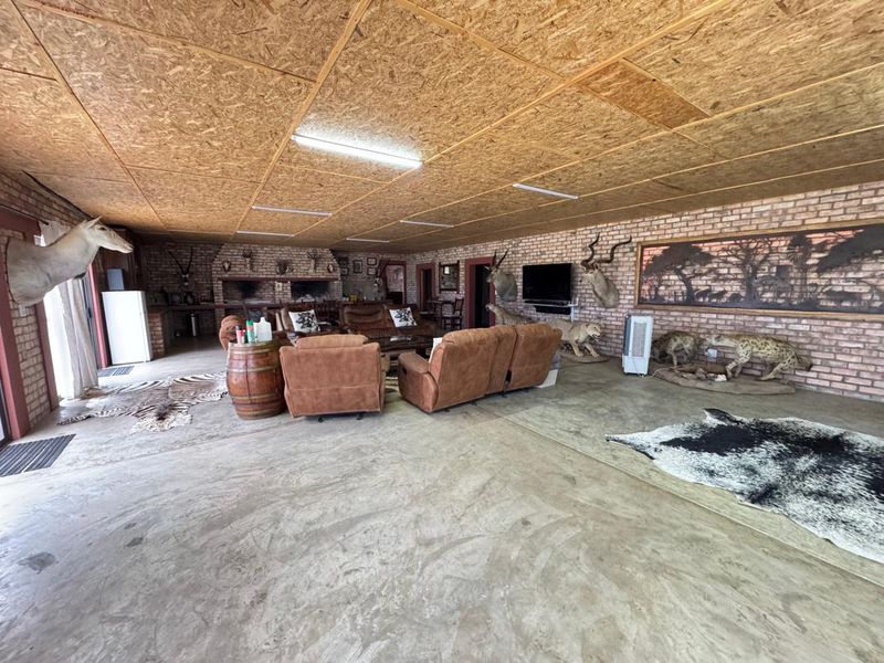 Spacious open-plan living area featuring exposed brick walls, a large built-in brick fireplace, and a unique OSB board ceiling with concrete flooring.
