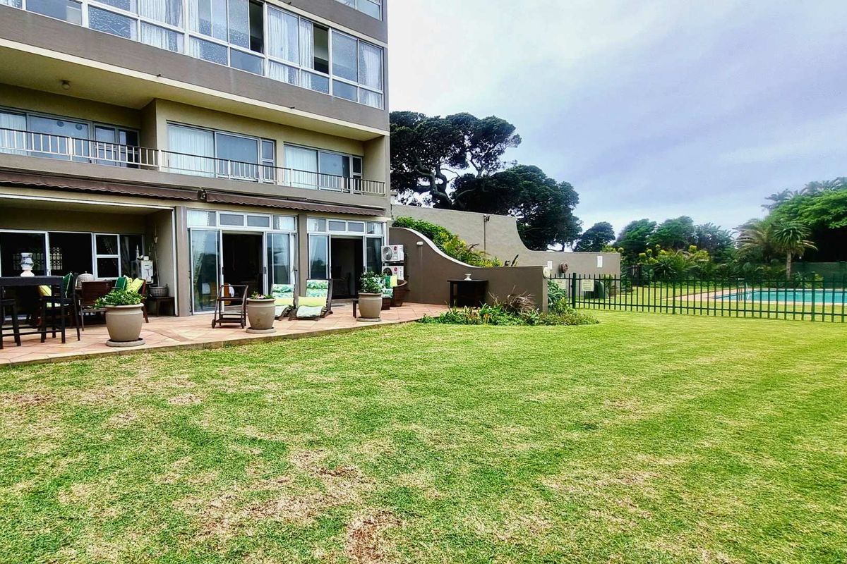 Rear view of the apartment building featuring a paved patio area, a spacious lawn, and direct access to the communal pool area.