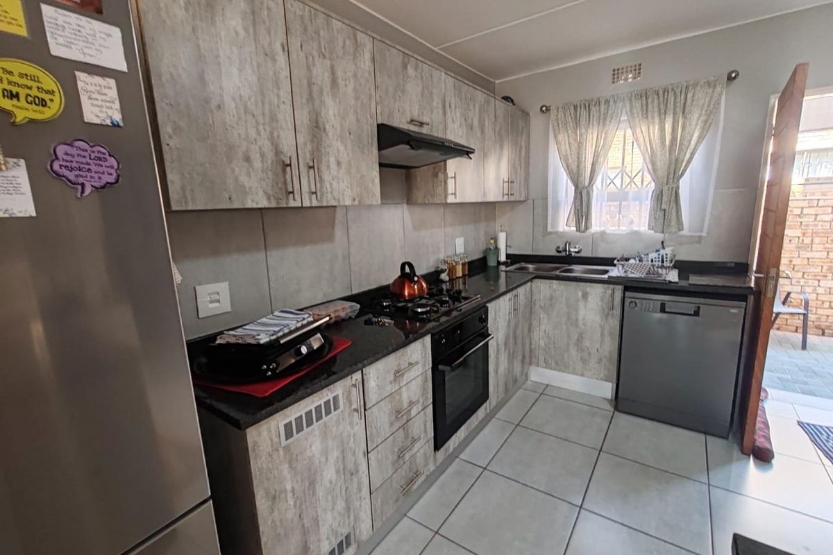 A functional kitchen featuring wood-look cabinetry, dark granite countertops, a built-in oven, gas hob, extractor fan, and a double sink with tiled flooring.
