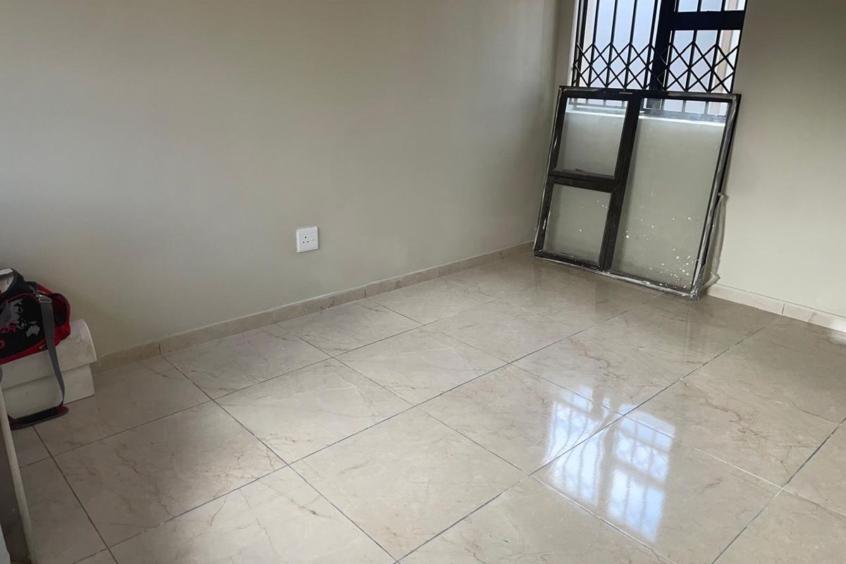 An empty bedroom featuring neutral wall paint, tiled flooring, and a window fitted with security bars.