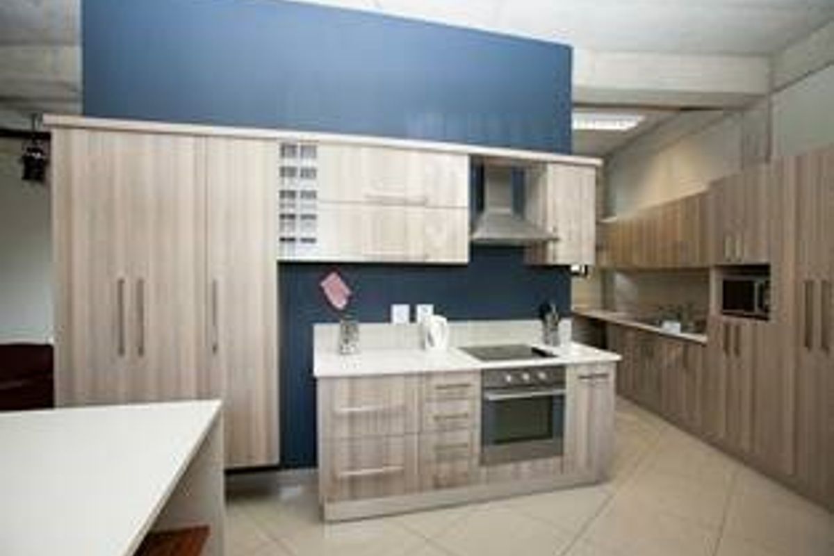 Modern kitchen featuring light wood-finish cabinetry, integrated appliances including an oven and hob, and tiled flooring with a contrasting blue feature wall.