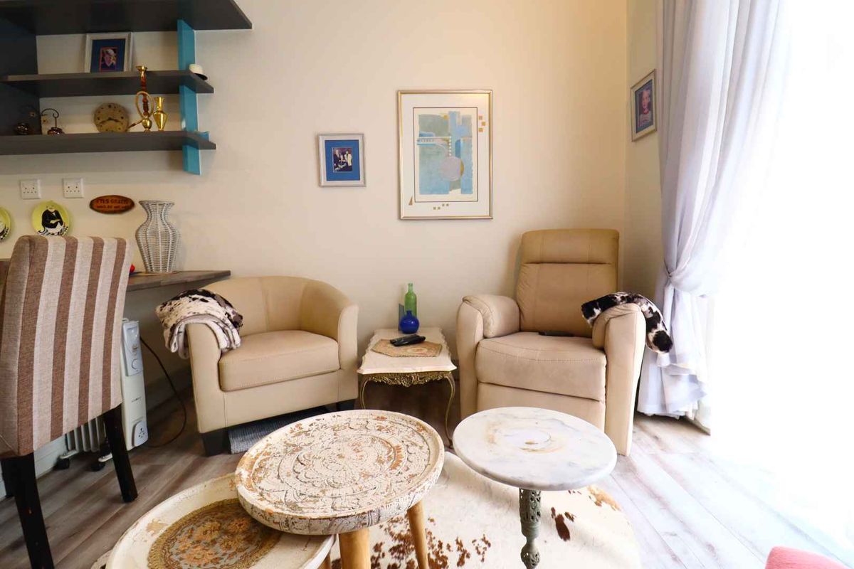 A cozy living area featuring light-toned laminate flooring, built-in wall shelving, and large windows with curtains allowing for natural light.