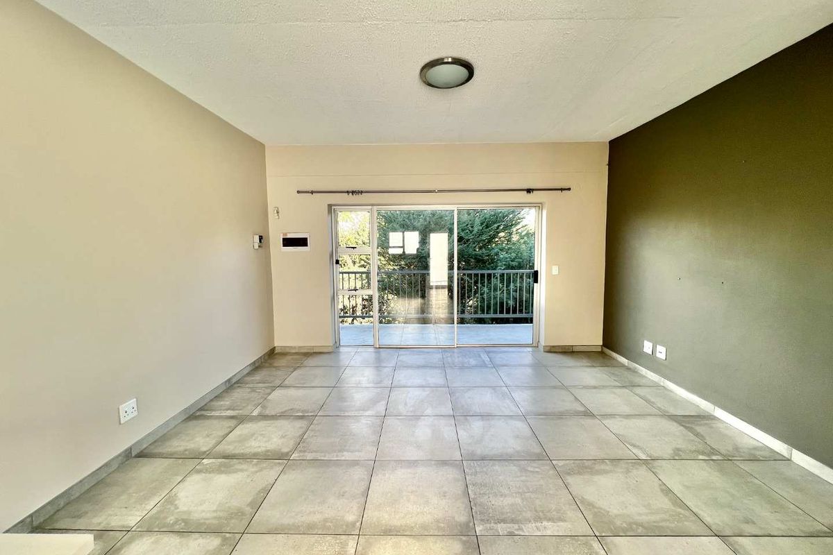 Spacious open-plan living area featuring large format floor tiles, a feature wall, and sliding glass doors leading to an outdoor balcony.