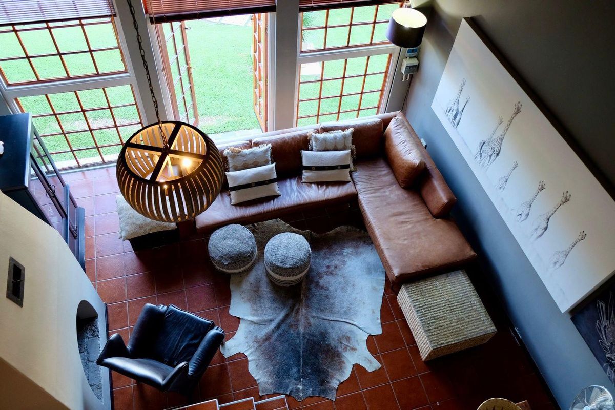 A high-angle view of a living room featuring terracotta floor tiles, a built-in fireplace, and large windows with direct access to the garden.