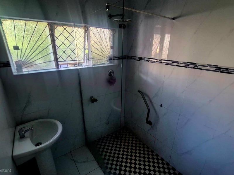 A functional bathroom featuring a pedestal basin, a walk-in shower with a glass screen, and tiled finishes throughout.