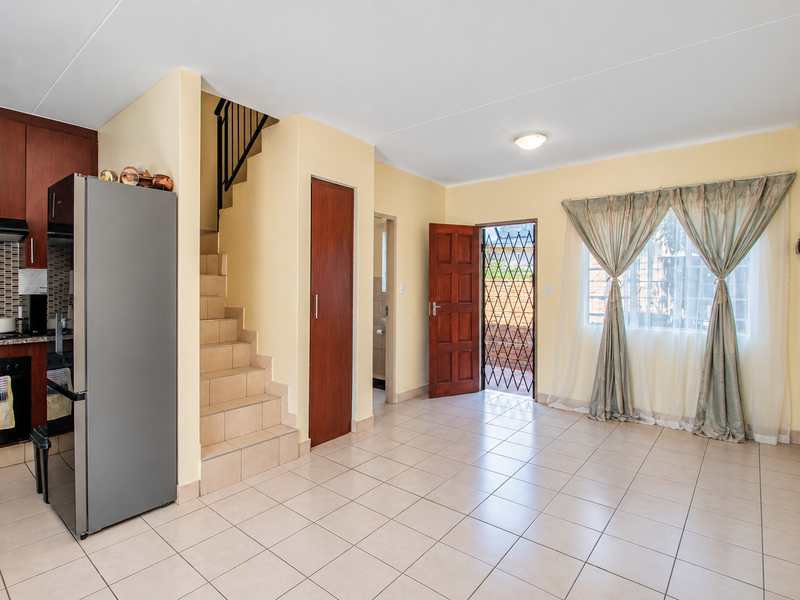 Open-plan living area featuring a functional kitchen with built-in cabinetry, tiled flooring, and direct access to the exterior via a security gate.