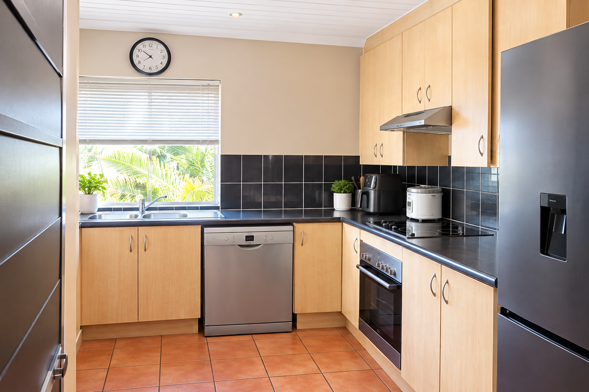 A functional kitchen featuring light wood cabinetry, black tile backsplash, dark countertops, and integrated appliances, offering a clean and practical workspace.