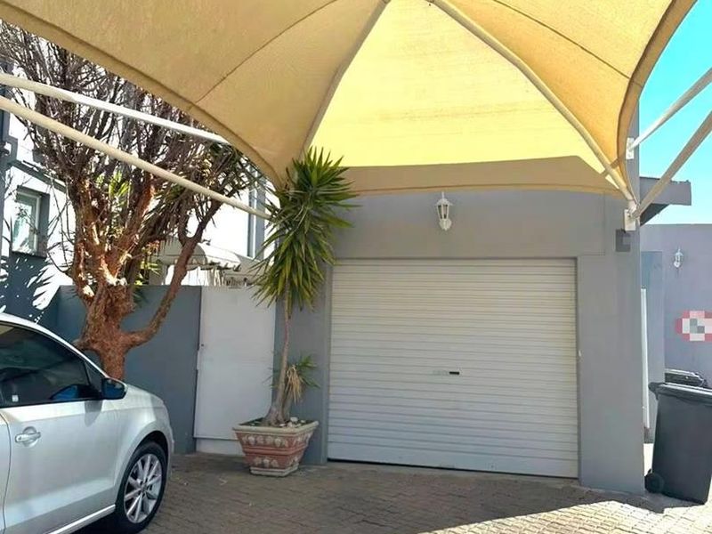A secure garage entrance featuring a roller shutter door and a protective shade sail structure over the paved driveway area.