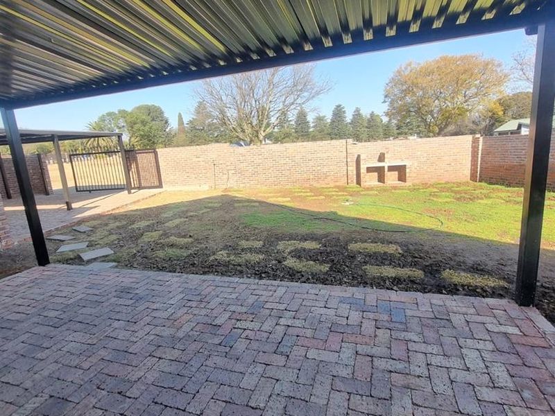 Covered patio area with brick paving, overlooking a private garden with a built-in braai and perimeter brick walling.