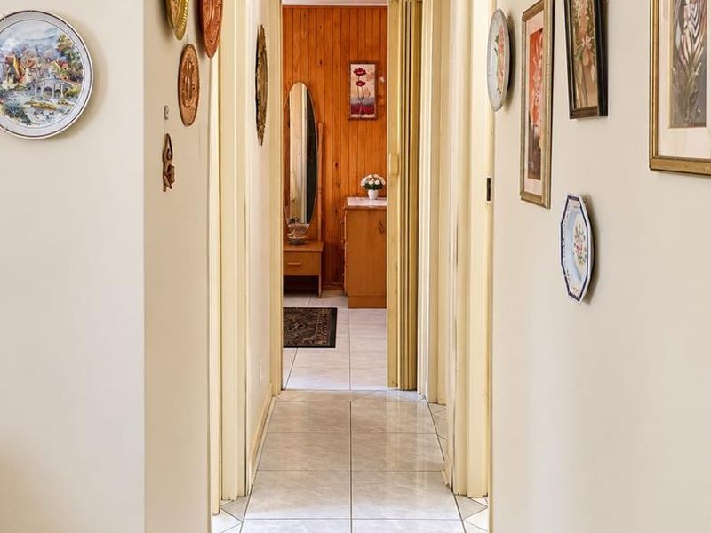 A well-lit hallway featuring neutral wall tones and light-colored floor tiles, providing access to adjacent rooms through standard and folding doors.
