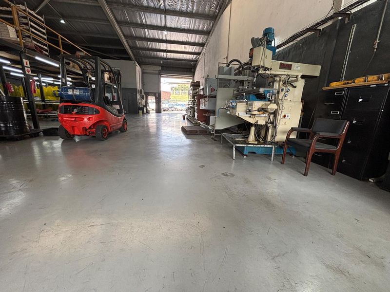 Spacious industrial warehouse unit featuring high ceilings, exposed steel trusses, and durable epoxy-coated concrete flooring, suitable for manufacturing or storage operations.