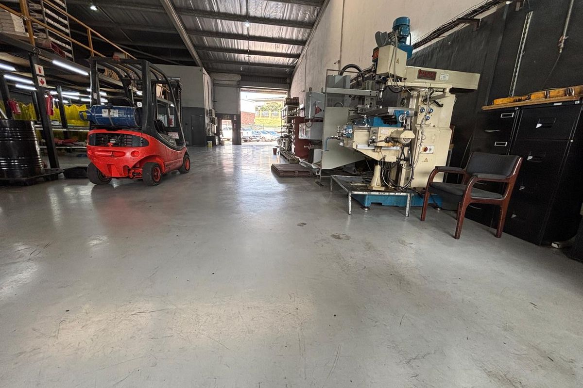 Spacious industrial warehouse unit featuring high ceilings, exposed steel trusses, and durable epoxy-coated concrete flooring, suitable for manufacturing or storage operations.