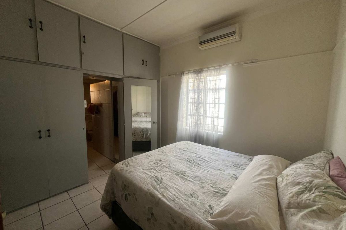 A bedroom featuring built-in cupboards, tiled flooring, and a wall-mounted air conditioning unit, with an adjoining en-suite bathroom.