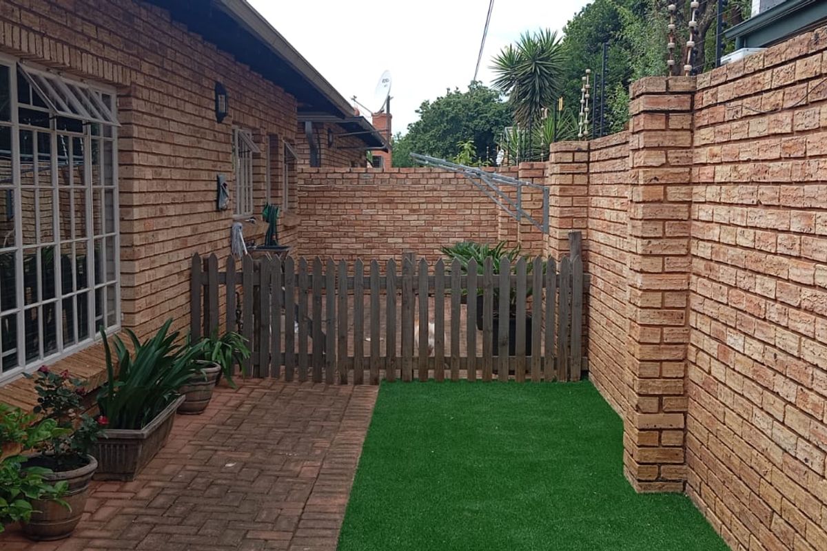 A private rear courtyard featuring face-brick walls, paved flooring, a small section of artificial lawn, and a secure wooden gate.